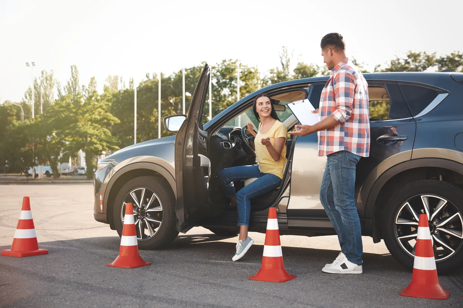 Fahrschule Two for You GmbH – Fahrlehrer mit Klemmbrett und sein Schüler neben einem Auto im Freien Fahrschulprüfung